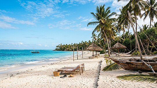 Strand mit weißem Sand, türkisfarbenem Wasser, Palmen, zwei Strohhütten, Liegestühlen, einer Tasche, Kamera und Hut im Vordergrund sowie einem hölzernen Boot mit der Aufschrift „Malawi“ am rechten Rand.