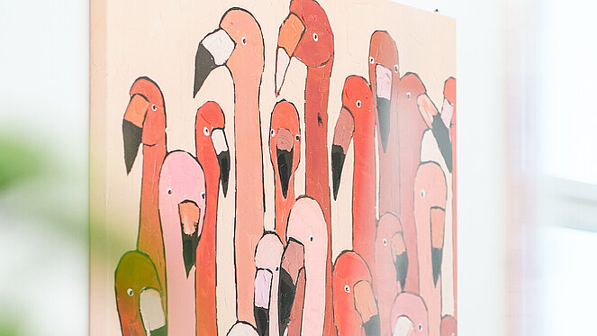 Illustration mit einer Gruppe stilisierter Flamingos in verschiedenen Rosa-, Rot- und Orangetönen. Die Vögel stehen dicht beieinander und füllen nahezu die gesamte Bildfläche. Das quadratische Gemälde hängt an einer hellen Wand in der Ordination der Tropenordination.